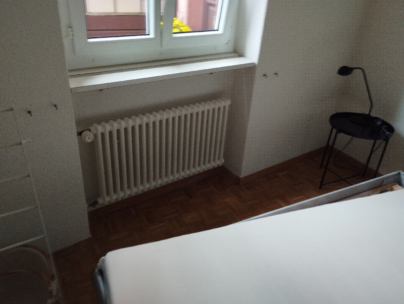 Im Schlafzimmer von Ormalingen deutet die ruhige Szene mit Bett und Heizung auf einen moeglichen Befall von Bettwanzen hin, der den Einsatz eines Kammerjaeger erforderlich machen koennte.