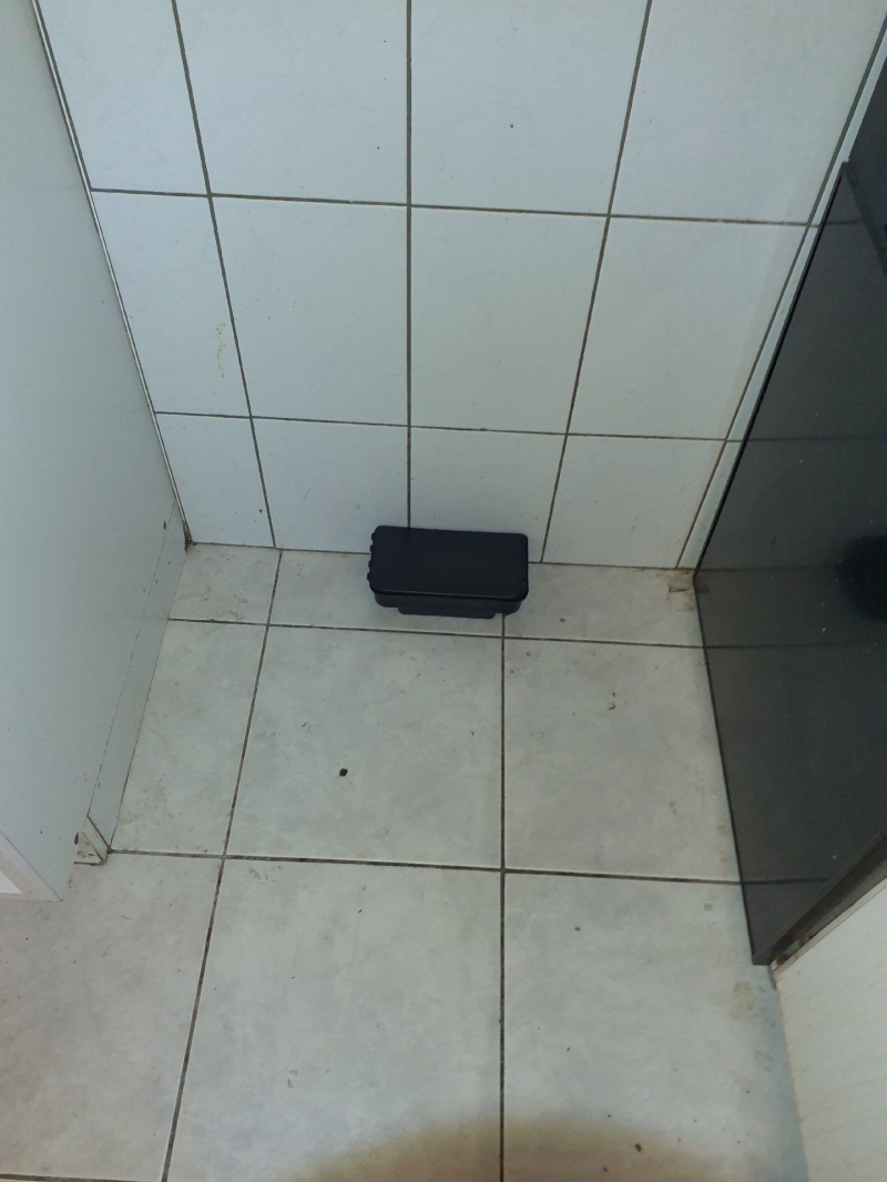 Auf den hellen Bodenfliesen in Arboldswil deutet die platzierte Koederbox auf einen vermuteten Rattenbefall hin, der den Einsatz eines Kammerjaegers erfordert.