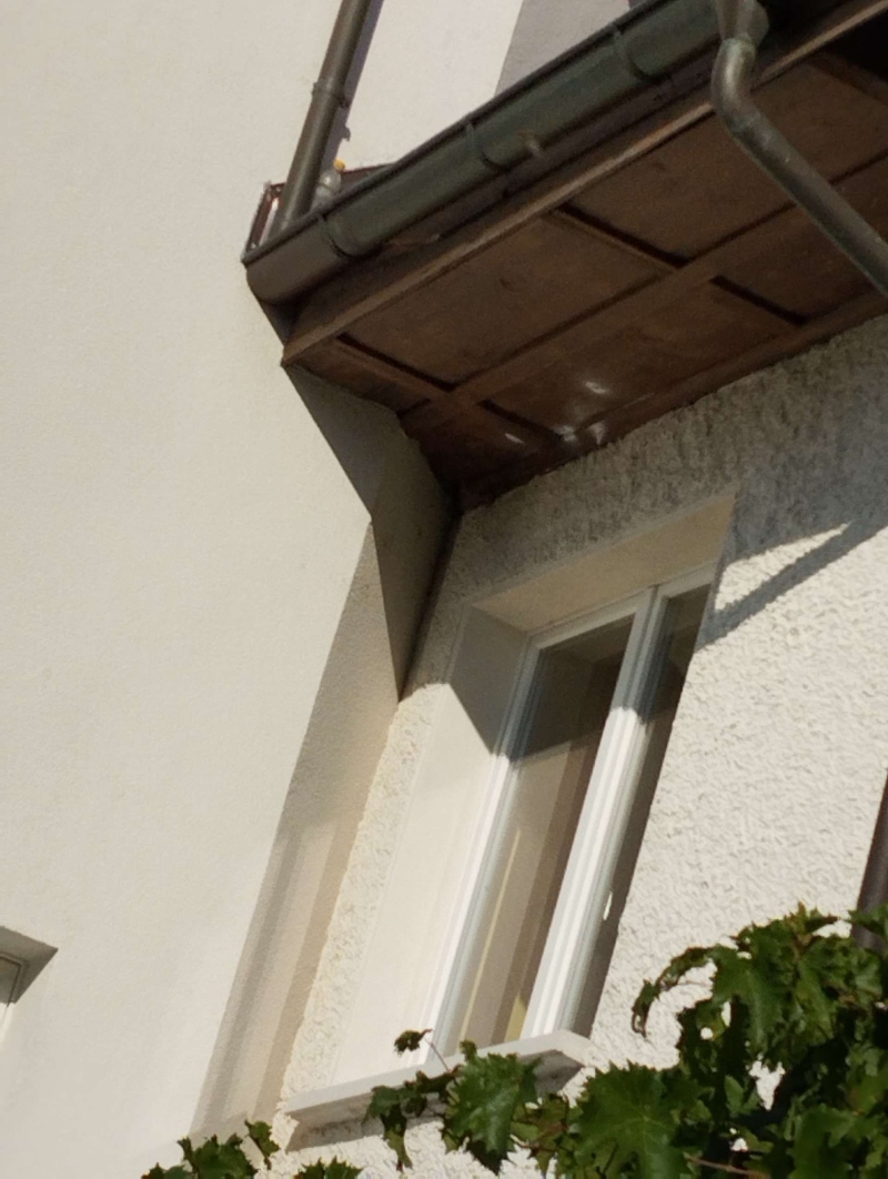Ein Kammerjaeger entdeckt in Aesch Spuren eines Wespennests unter dem Dachvorsprung nahe eines Fensters, wo sich dunkle Rueckstaende an der Holzverkleidung zeigen.
