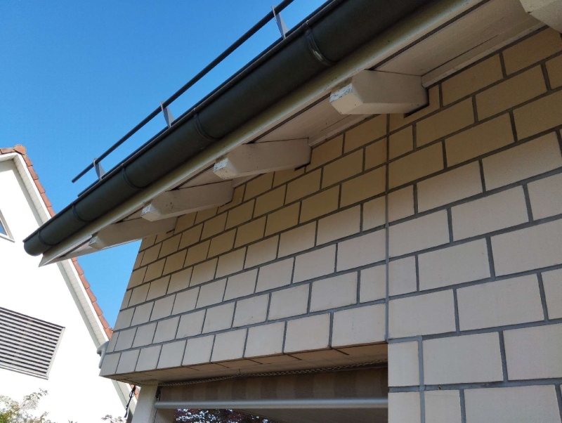 An den hellen Mauersteinen unter dem Dachvorsprung in Birsfelden weist ein geschuetzter Winkel auf ein moegliches Hornissennest hin, das den Einsatz eines Kammerjaegers erfordert.