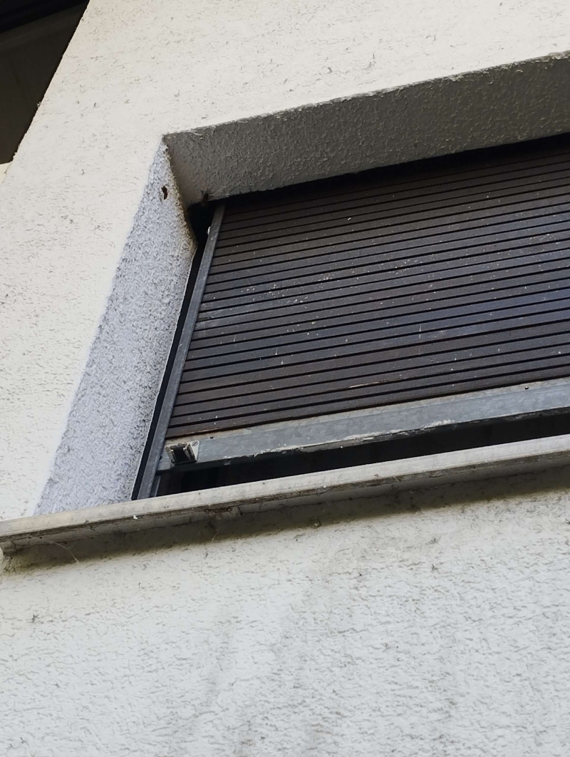 Unter einem halb geoeffneten Rollladen in Ruenenberg weist ein verdeckter Spalt auf ein moegliches Hornissennest hin, das den Einsatz eines Kammerjaegers notwendig macht.